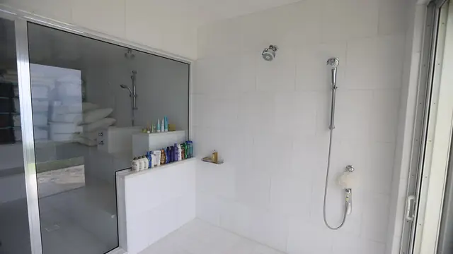 Bathroom Renovation work: USVI IMG 5251 - Clean white tiles modern shower with handheld nozzle and glass enclosure neatly arranged toiletries on the wall